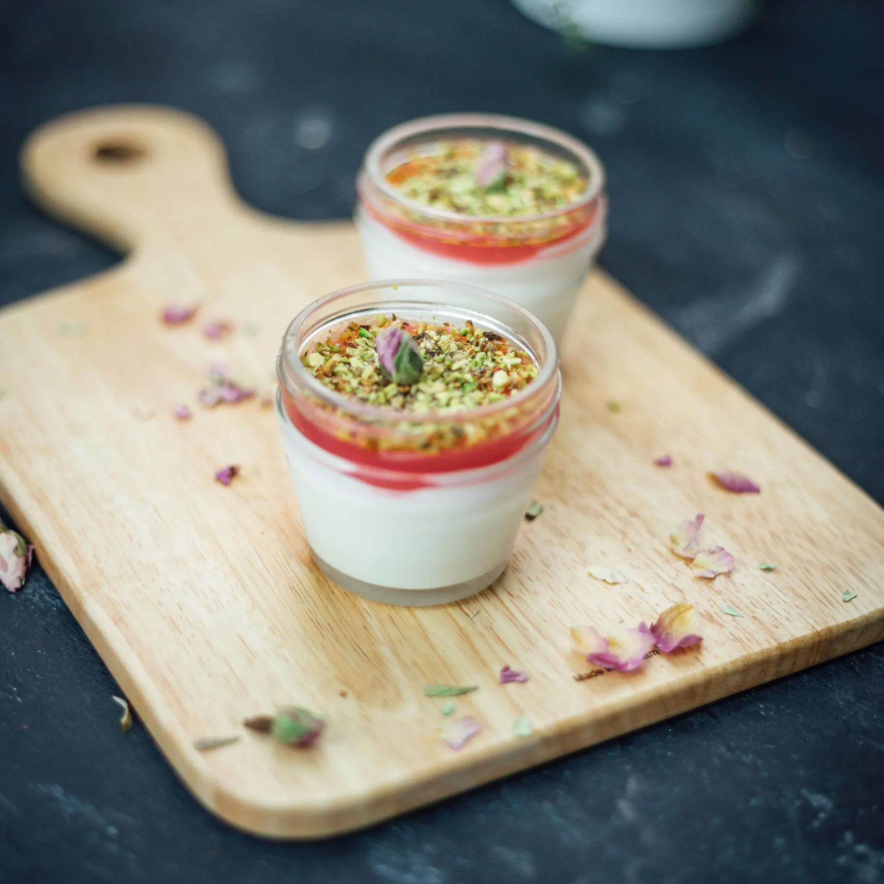 Two farni jars topped with pistachio and rose, on a wooden board